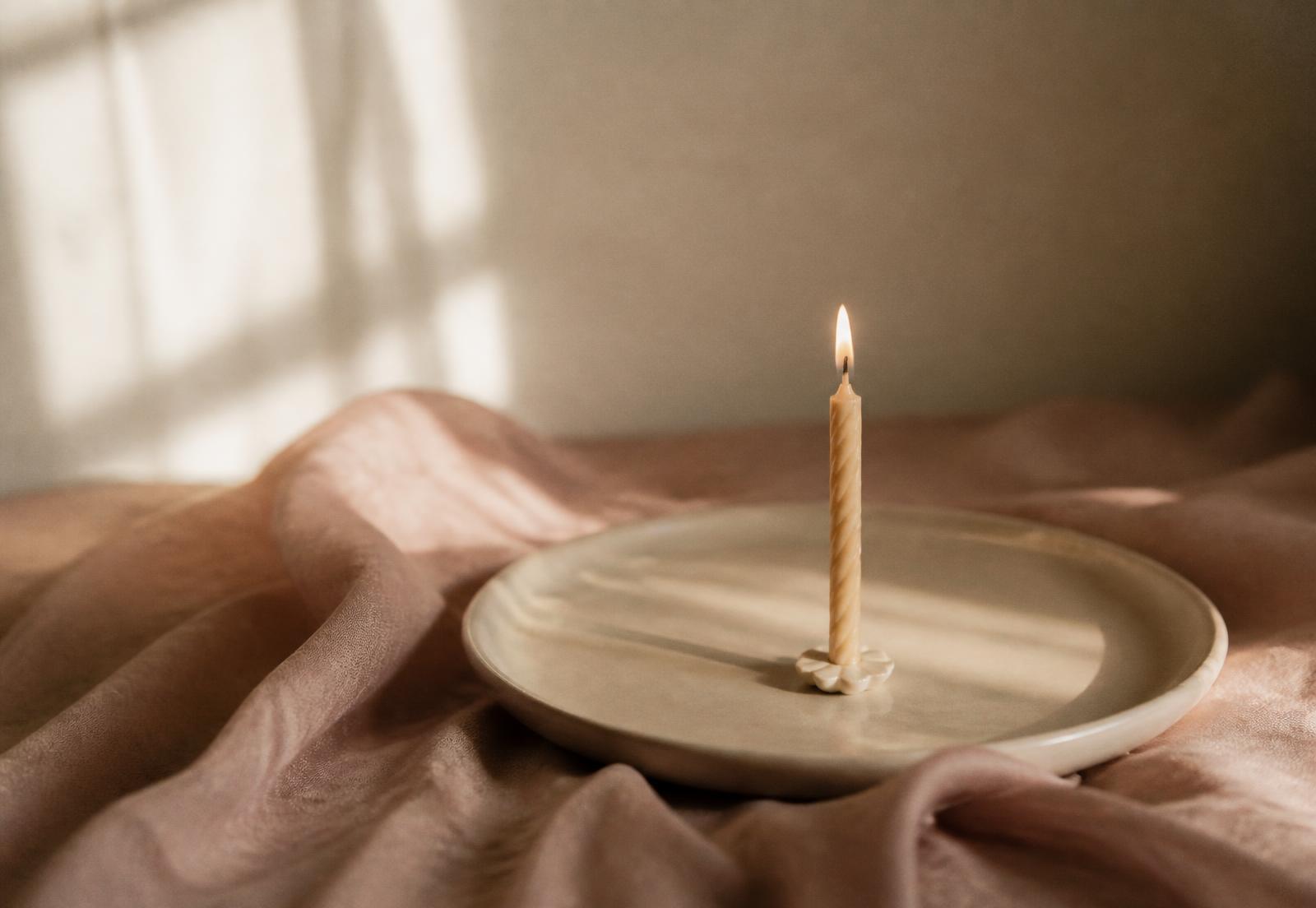 Single lit candle on a ceramic plate with blush linen