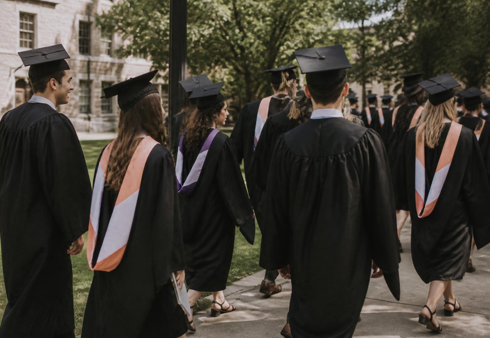 Graduates walking across campus in caps and gowns